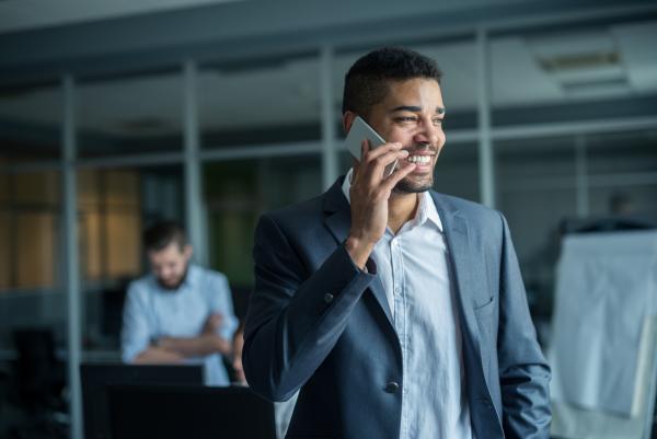 Man in dress shirt smiling while holding a cellphone to his ear