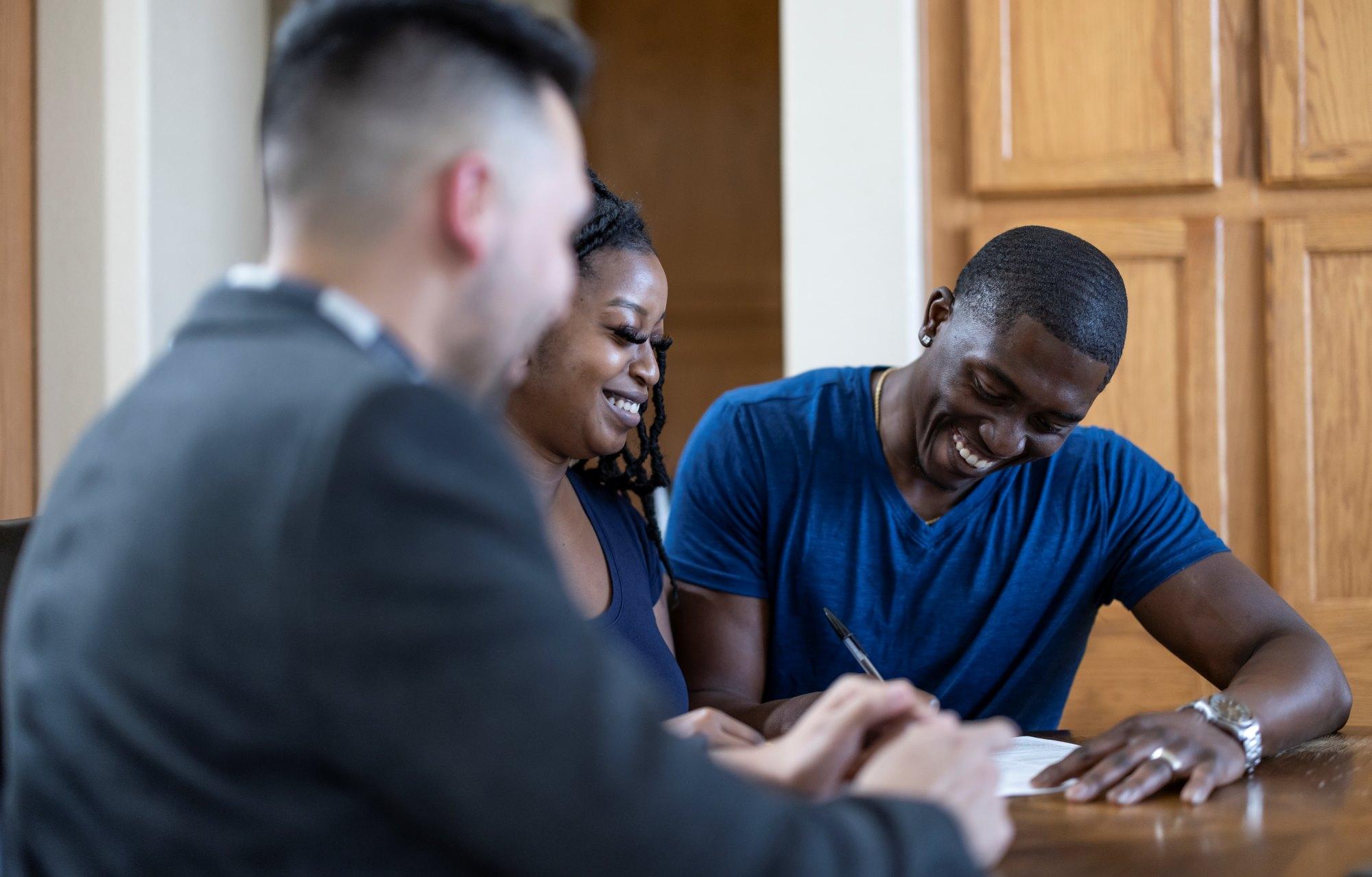 Couple sitting at table signing a document and smiling.
